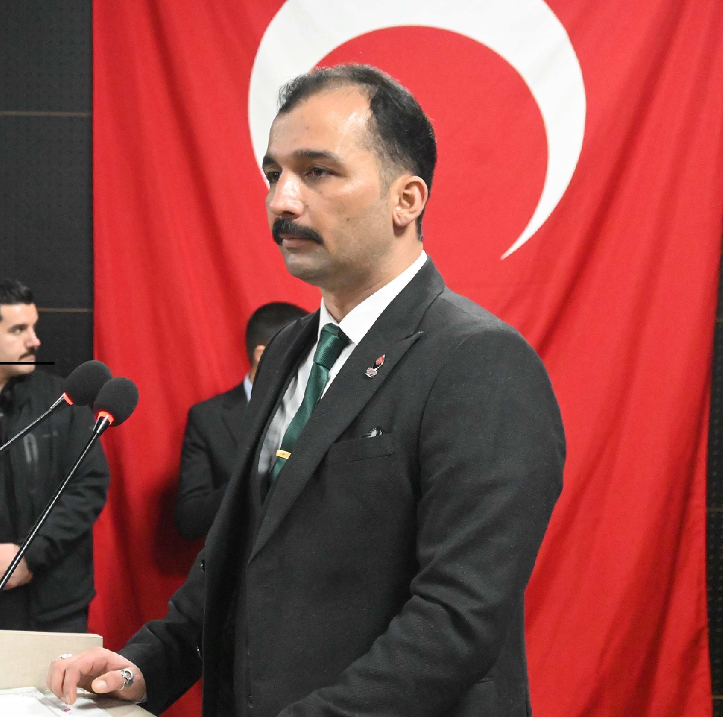 Hacı Filik Türk bayrağı önünde kürsüde konuşurken